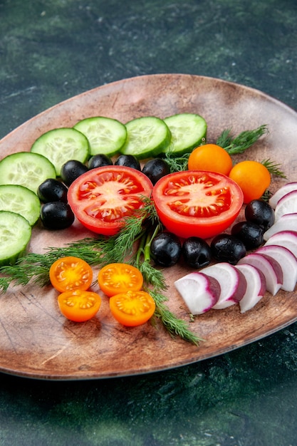 Vertical view of fresh chopped vegetables olives kumquats in a brown plate on green black mixed colors background