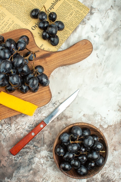 Vertical view of fresh delicious black grape bunch and cheese on wooden cutting board and in a brown pot knife on mixed color background