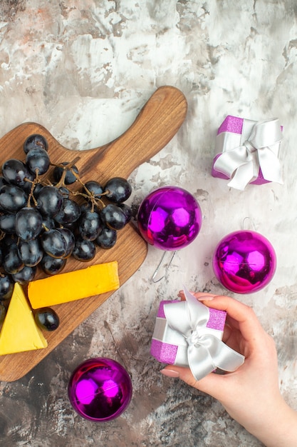 Vertical view of fresh delicious black grape bunch and cheese on wooden cutting board and hand holding gift decoration accessories on mixed color background