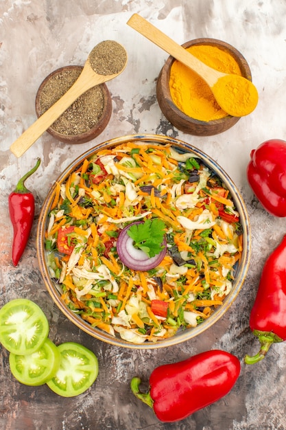 Vertical view of fresh delicious vegan salad of various organic vegetables and red peppers next to different spices with spoons