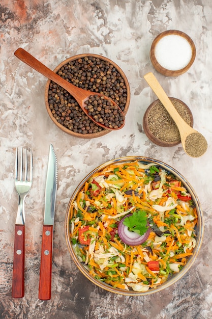 Free photo vertical view of fresh delicious vegan salad of various organic vegetables with knife and fork and various spices