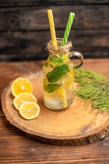 Vertical view of fresh detox water in a glass served with tubes and lemon limes on a brown tray