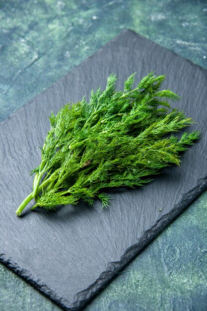 Vertical view of fresh dill bundle on black cutting board on green black mix colors background