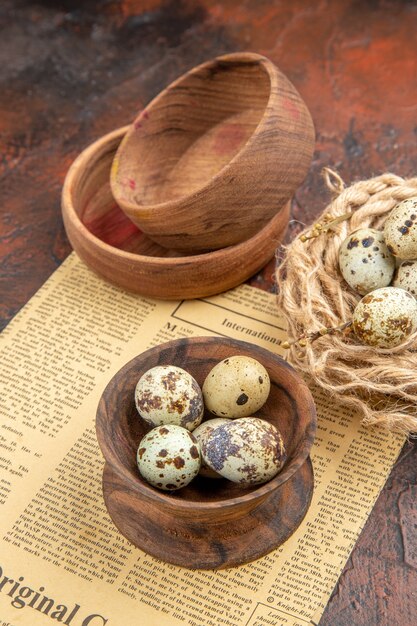 Vertical view of fresh eggs from a basket with towel and old newspaper wooden pots on a brown background