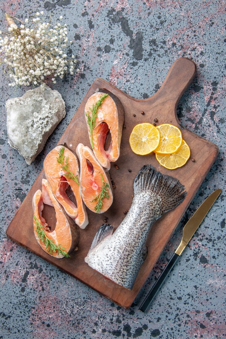 Free Photo vertical view of fresh fishes lemon slices greens pepper on wooden cutting board and knife on blue black mix colors table