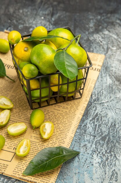 Vertical view of fresh kumquats and lemons in a black basket on newspapers on gray background