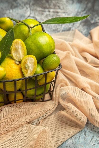 Vertical view of fresh kumquats and lemons in a black basket on towel on gray background