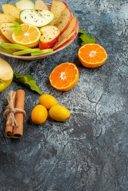 어두운 배경의 오른쪽에 레몬과 계피 라임 금귤 오렌지가 있는 흰색 접시에 있는 신선한 천연 사과 조각의 수직 보기
