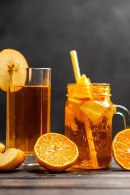 Вертикальный вид свежего натурального вкусного сока в двух стаканах, рука положить фруктовый лайм с трубкой в нем на черном фоне
