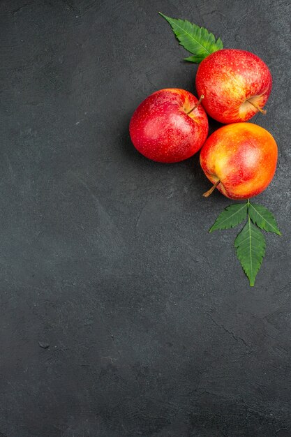 Vertical view of fresh natural organic red apples with green leaves on black background