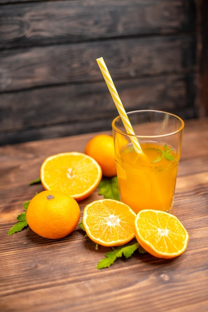 Вертикальный вид свежего апельсинового сока в стакане с мятой и целыми апельсинами слева на деревянном столе