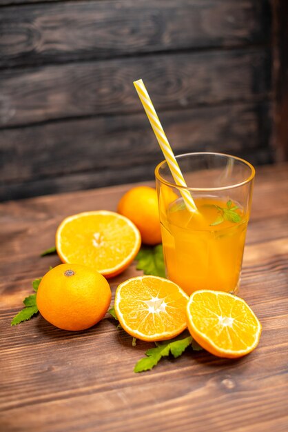 ガラスのフレッシュ オレンジ ジュースの垂直方向のビューは、木製のテーブルの左側にチューブ ミントと丸ごとカット オレンジを添えて