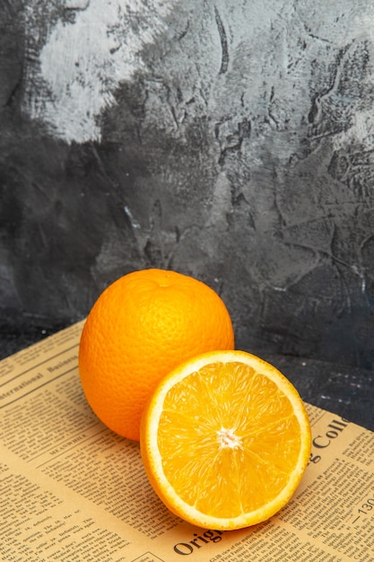 Vertical view of fresh oranges in cut and whole form on newspaper on gray background