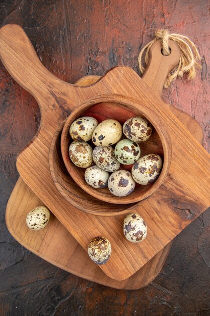 Free photo vertical view of fresh organic poultry farm eggs in a wooden bowl on a cutting board on brown background