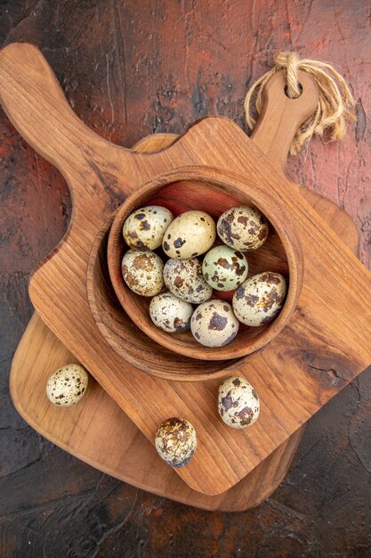 Vertical view of fresh organic poultry farm eggs in a wooden bowl on a cutting board on brown background