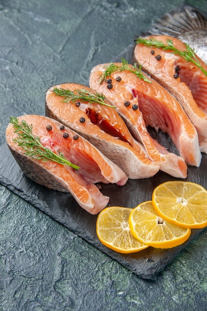 Vertical view of fresh raw fishes greens pepper and lemon slices on dark color tray on blue black mix colors table