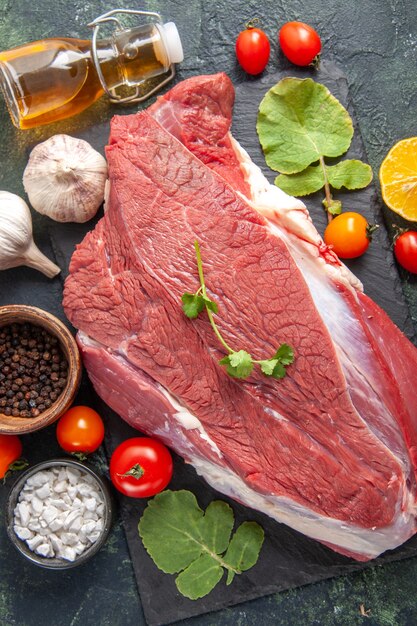 Vertical view of fresh raw red meat on black tray pepper vegetables fallen oil bottle knife on dark color background