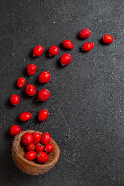 Vertical view of fresh red cornel berries pouring out brown bowl on black