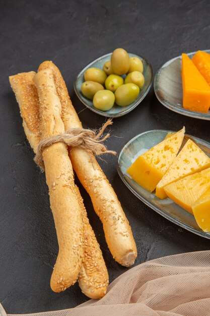 Vertical view of fresh tasty chees slices on a towel and green olives on a black background