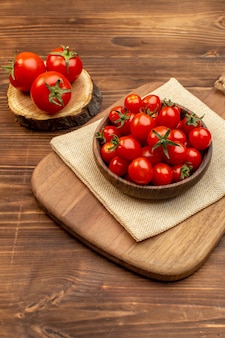 Vertical view of fresh tomatoes on a brown bowl on cutting board on wooden board spices with free space