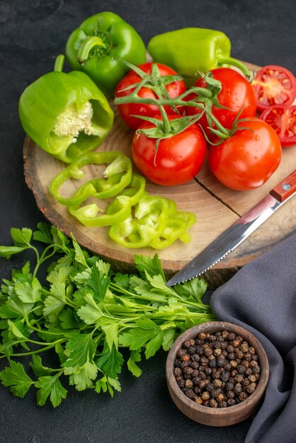 Vertical view of fresh tomatoes and green peppers on wooden board green bundle on black surface