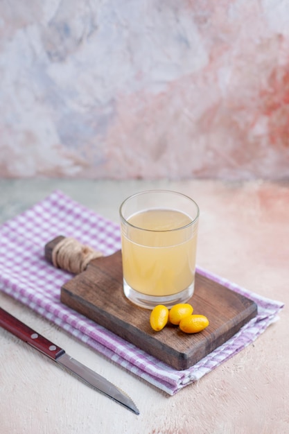 Vertical view of fruit juice on wooden cutting board on purple stripped towel on pastel colors background