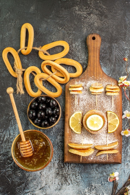 ボウルの蜂蜜と灰色のテーブルの上のブラックチェリーの近くのフルーツパンケーキクッキーの垂直方向のビュー