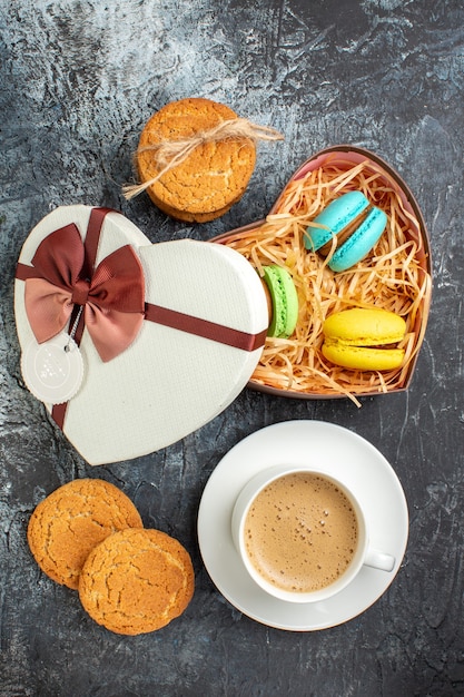 Vertical view of gift box with macarons and cookies a cup of coffee on icy dark background