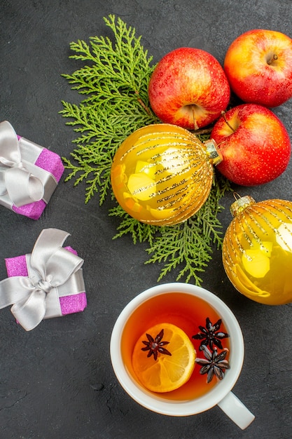 Vista verticale di regali e mele fresche biologiche naturali e accessori decorativi una tazza di tè su sfondo nero