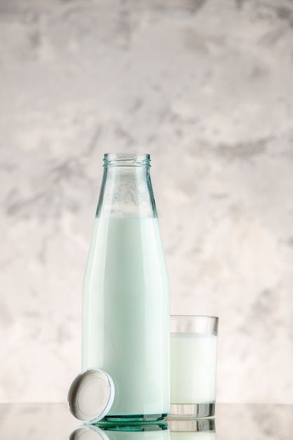 Vertical view of glass bottle and cup filled with milk cap on white smoke background with free space