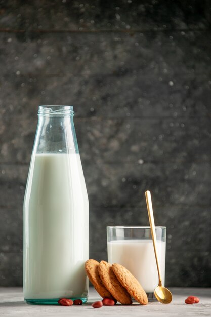 Vertical view of glass bottle cup filled with milk and peanuts on gray table on wooden background