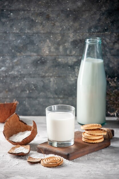 Vertical view of glass bottle and cup filled with milk on wooden tray flower on dark background