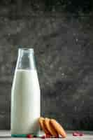 Foto gratuita vista verticale della bottiglia di vetro riempita di latte e arachidi sulla tavola grigia su fondo di legno
