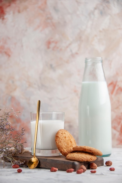 혼합 색상 표면에 있는 나무 보드 꽃에 우유 쿠키로 채워진 유리 컵과 병의 수직 보기