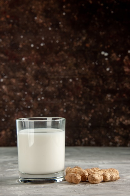 Вертикальный вид стеклянной чашки, наполненной молоком и сухофруктами на темном фоне