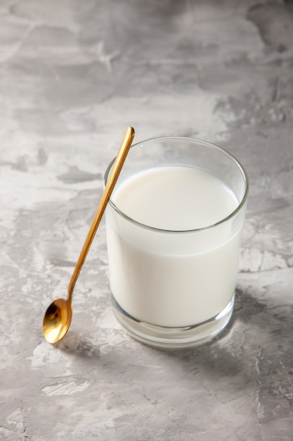 Foto gratuita vista verticale della tazza di vetro piena di latte e cucchiaio d'oro sul tavolo grigio con spazio libero