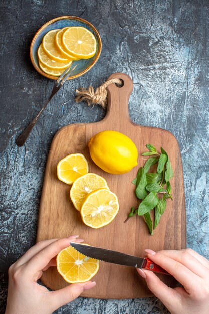 暗い背景に木製のまな板の上に新鮮なレモンとミントを刻む手の垂直方向のビュー