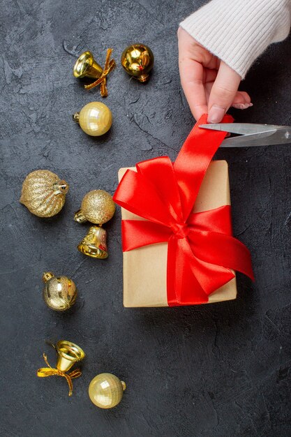 Vertical view of hand cutting red ribbon on gift box and decoration accessories on dark background