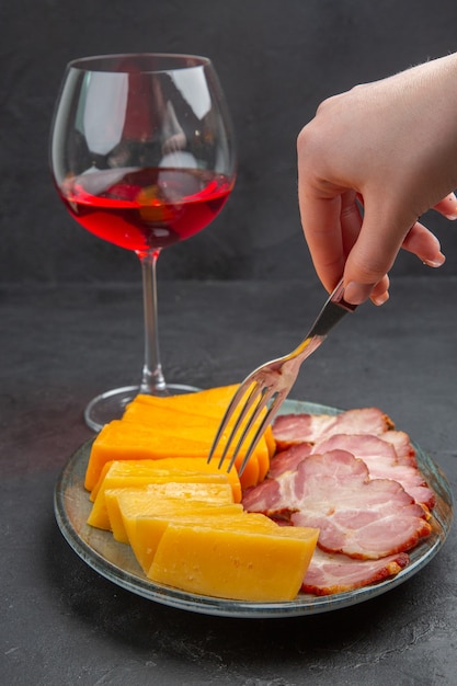 Vertical view hand holding fork on a blue plate with delicious snacks and red wine in glass