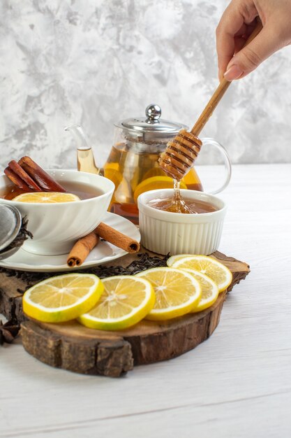 Vertical view of hand holding tea spoon with honey black tea in a white cup on white table