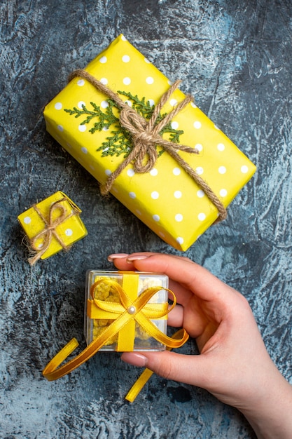 어두운 배경에서 작은 선물 상자와 다른 두 개의 크리스마스 선물 상자를 여는 손의 수직 보기