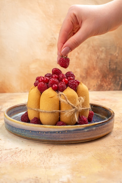 Vertical view of hands holding a strawberry on freshly baked soft cake with fruits