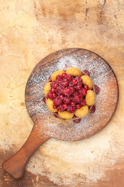 Vertical view of homemade soft cake with fruits on wooden cutting board on mixed color table