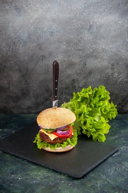 Vertical view of knife in delicious meat sandwich and green on black tray on the left side on blurred surface