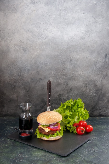 Vertical view of knife in delicious meat sandwich and green pepper on black tray sauce ketchup tomatoes with stem on gray surface