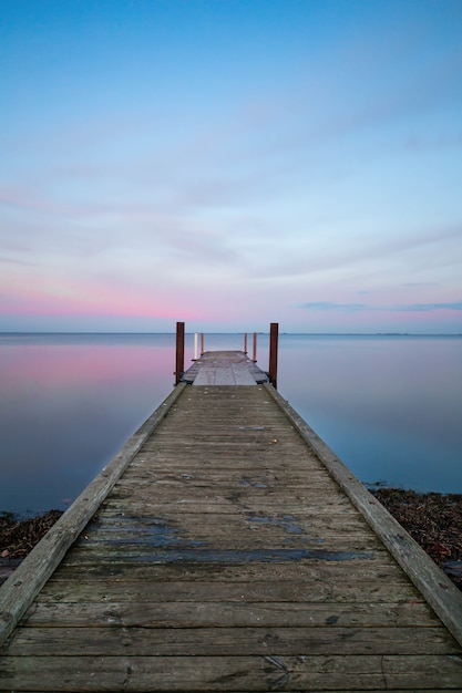 Foto gratuita vista verticale di un lungo molo in legno vicino all'oceano sotto il cielo color pastello