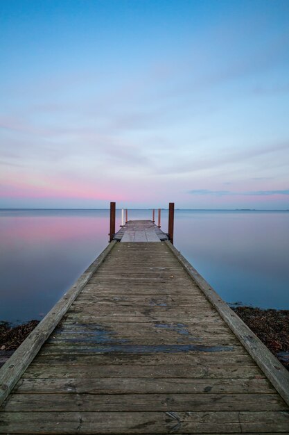 Vertical view of a long wooden pier near the ocean under the pastel-colored sky