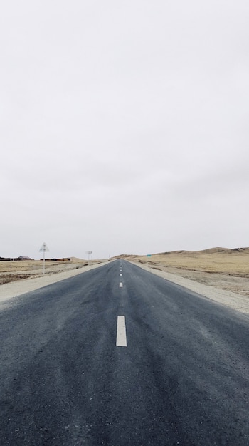 澄んだ空の下のフィールドの真ん中にある狭い道路の垂直方向のビュー