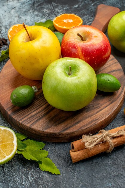 Vertical view of natural fresh apples lemon on wooden cutting board and cinnamon limes kumquats oranges on dark table