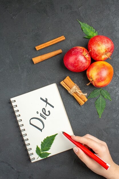 Vertical view of natural organic fresh apples with green leaves cinnamon limes notebook with diet inscription on black background